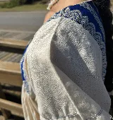 Túnica de lino color crudo con corte holgado y mangas cortas. Presenta una pechera cuadrada en el frente y la espalda confeccionada con textiles antiguos en color azul con patrones geométricos de ondas.
