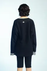 Buzo de felpa negro de corte oversize, con cuello redondo y mangas largas con puños grises doblados hacia afuera. Presenta costuras externas decorativas en tono gris claro a lo largo de las mangas y los hombros.