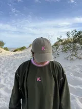 Gorro de estilo gorra de béisbol, color beige desgastado, con una letra "K." bordada en color rosa en el frente.