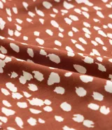 Vestido corto amplio color ladrillo con lunares irregulares color crema, cuello redondo con lazo, mangas largas con puños anchos y bajo fruncido.