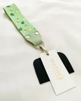 Llavero de tela con estampado de aguacates, detalles en cuero sintético verde y gancho metálico plateado.