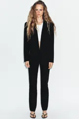 Blazer corto de corte recto con cuello de solapa, manga larga y hombreras. Presenta un diseño minimalista sin botones y forro interior a tono.