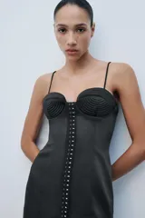 Vestido corto satinado negro con escote corazón, tirantes finos y cierre frontal con corchetes metálicos.
