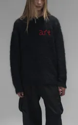 Sweater de punto negro con textura suave, cuello redondo y diseño oversize. Presenta un bordado frontal con la frase 'art SUPPORT' en letras rojas y blancas, y un pequeño detalle de tijeras bordado en la nuca.