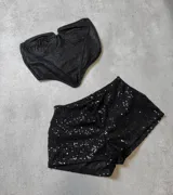 Conjunto de dos piezas compuesto por un corset strapless de tela brillante con estructura de copas y un short de lentejuelas negro con cintura elástica.
