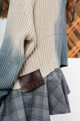Saco de hilo con cuello alto y cierre de botones, de tejido de punto y diseño oversize. Presenta un teñido artesanal degradado que combina gris y beige, con mangas largas y puños amplios, además de un detalle de aplicación floral oscura en el pecho.