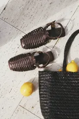 Sandalias planas tipo huarache de cuero negro, con tiras entrelazadas a mano y tira ajustable en el talón con hebilla metálica.