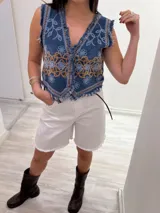 Chaleco corto en denim azul con detalle desflecado y bordado artesanal en tonos celeste y dorado. Estilo boho chic con escote en V, ideal para combinar con prendas básicas y elevar tu look.