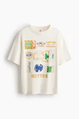 Remera oversized de algodón color blanco, con cuello redondo y diseño estampado en el frente con motivos de paquetes de mantequilla y la palabra "BUTTER".