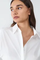Camisa de manga larga confeccionada en popelina de algodón, con diseño de corte recto, cuello clásico, cierre frontal oculto y puños anchos con botón.