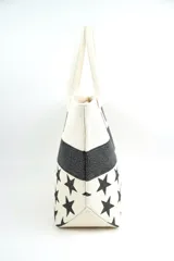 Bolso tipo tote color beige con estampado de estrellas negras, franja superior con brillos negros y asas de hombro en tono crudo.