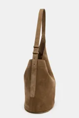 Bolso tipo saca de diseño asimétrico confeccionado en piel de ante. Cuenta con un asa bandolera ajustable, cierre mediante imán y un bolsillo interior con cremallera.