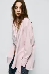Camisa de corte oversize con cuello solapa y escote en pico. Presenta manga larga con puños abotonados, cierre frontal con botones y detalle de lazada ajustable en la espalda.