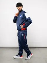 Conjunto deportivo Umbro del Club Nacional de Football, compuesto por una campera con cierre frontal y un pantalón a juego. Ambas piezas son de color azul marino con detalles en blanco y rojo, presentando el escudo del club y el logo de la marca.
