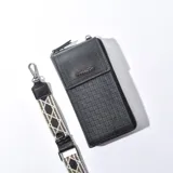 Porta celular negro con textura tejida, solapa con cierre a presión y logo de la marca en el frente. Incluye correa de tela estampada con motivos geométricos.