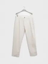 Pantalón de vestir color crema, confeccionado en tejido ligero de algodón con textura seersucker. Tiene corte recto, bolsillos laterales y traseros, cierre con botón y cremallera, y parche con logo de la marca.