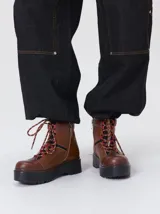 Bota de estilo trekking con diseño multicolor en tonos marrón, azul y detalles en rojo. Presenta plataforma de goma dentada, cordones tipo cuerda de escalada y cuello acolchado.