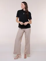 Blusa blanca de corte recto con cuello alto torzado, abertura frontal en gota y mangas cortas con aberturas sobre los hombros.