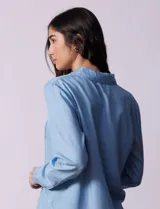 Camisa celeste de lyocell, con cuello a la base, escote en V y abertura central con botones. Tiene bolsillos aplicados en la parte delantera y mangas 3/4 regulables con presilla y botón.