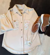 Sobre camisa beige de manga larga, con bolsillos en el pecho y detalles de tela guardamonte en los bolsillos y puños.