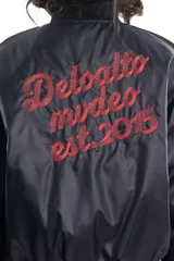 Campera bomber negra de tela satinada con bordado rojo en el pecho. Es reversible.