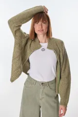 Cardigan tejido de punto grueso color gris claro con diseño de trenzas, cuello alto y cierre frontal con cremallera.