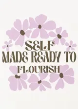 Remera de algodón color blanco, con cuello redondo y mangas cortas. Presenta un estampado frontal con flores en tonos lila y la frase "Self made ready to flourish" en letras negras.