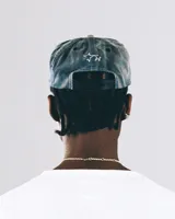 Gorro tipo gorra de béisbol de tela lavada color azul grisáceo, con visera curva y cordón decorativo negro en la base de la visera. Presenta un bordado frontal con la palabra "TWOJEYS" y la silueta de un caballo salvaje.