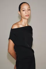 Vestido midi negro confeccionado en hilatura de viscosa, de diseño satinado y corte asimétrico con escote fluido y manga sisa. Presenta bajo acabado en línea evasé y cierre lateral con cremallera oculta en costura.