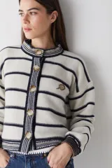 Cardigan de lana color bordó con cuello redondo, cierre frontal de botones y mangas largas. Presenta detalles de ribetes en contraste en cuello, puños y borde inferior, además de un bordado de raqueta de tenis en el pecho.