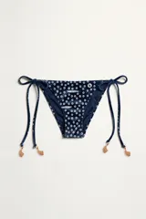 Bombacha de bikini azul marino con estampado geométrico de círculos y tiras laterales ajustables. Confeccionada en tejido jacquard con hilos metalizados, ofrece protección UV50 y resistencia al cloro y protectores solares.