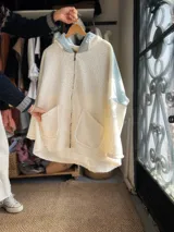 Campera de estilo oversize confeccionada en una combinación de corderito blanco y denim celeste. Presenta un diseño frontal con un aplique bordado de sol en tonos tierra y una etiqueta de marca en el centro. Posee mangas largas y cuello alto.