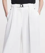 Pantalón de corte amplio tipo pantalona, confeccionado en tejido plano de poliéster. Presenta cintura alta con cinturón elástico integrado que incluye hebilla metálica, pliegues frontales y bolsillos laterales.