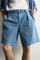 Bermuda de denim con corte relaxed fit, tiro medio y pierna recta. Presenta pliegues frontales dobles, bolsillos laterales y bolsillos traseros de doble vivo. Confeccionada en tejido rígido con efecto lavado, cierre frontal con cremallera y botón.