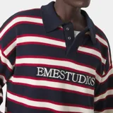 Sweater de punto color azul marino con rayas horizontales blancas y rojas. Tiene cuello polo, abertura en el escote y el logo "EMESTUDIOS" bordado en el pecho. Presenta un corte corto.