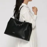 Cartera tipo tote de cuero sintético negro con doble asa de hombro, costuras en contraste y una cadena decorativa frontal con los dijes que forman la marca. Cuenta con logo impreso en la parte inferior.