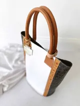 Bolso matero blanco con laterales en cuero negro con textura de cocodrilo, manijas de cuero color suela y accesorio metálico plateado en forma de cruz.