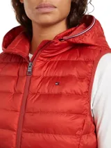 Chaleco acolchado rojo con capucha extraíble, cierre de cremallera, dos bolsillos delanteros con cremallera y logo de Tommy Hilfiger bordado en el pecho.