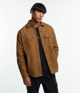 Camisa de manga larga color marrón, confeccionada en sarga de algodón, con cuello inglés, botones frontales y dos bolsillos de parche con solapa y botón en el pecho.