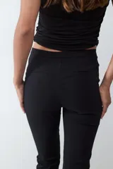Pantalón recto cropped negro de tiro medio y fit slim, confeccionado en tejido elasticado. No tiene bolsillos visibles y cuenta con cierre frontal oculto.