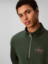 Buzo Calvin Klein de felpa color verde oscuro, con cuello alto, cierre frontal parcial de un cuarto y manga larga. Presenta el logo de la marca bordado en el pecho.