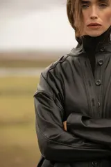 Mameluco negro de cuero ovino, con cuello alto, cierre frontal con botones a presión, cinturón con hebilla forrada y bolsillos laterales.