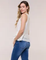Blusa blanca sin mangas confeccionada en tejido de satén con suave textura arrugada y caída fluida. Cuenta con escote en V con volante en el cuello y ruedo estilo peplum con doble capa de volados superpuestos.