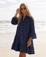 Vestido corto de lino azul marino, de corte amplio y diseño escalonado con volados. Cuenta con mangas largas terminadas en volados y cierre frontal con botones de coco.