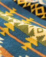 Buzo polar de cuello alto con cierre frontal de botones a presión, confeccionado en fleece sintético. Presenta un estampado geométrico multicolor con predominancia de tonos azules, amarillos y verdes. Incluye un bolsillo frontal tipo cargo con solapa y cierre de botón, además de bolsillos laterales ocultos.
