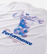 Remera de algodón color blanco tiza, manga corta y cuello redondo. Presenta un estampado grande en la espalda con la palabra "Creative" en tipografía cursiva iridiscente, un oso de goma con efecto holográfico en tonos azules y rosados, y el texto "MATTERS MORE THAN P¡FORMACE" debajo.