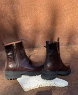 Botas de cuero con textura simil cocodrilo en color marrón, diseño de caña baja con cierre lateral y suela track negra de goma.