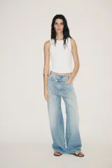 Jeans de tiro alto, color gris oscuro lavado, con pierna ancha extra larga (full length) y diseño de cintura cruzada asimétrica con cierre frontal de cremallera y botones metálicos.