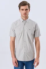 Camisa de manga corta de algodón en color celeste con microdiseño geométrico a cuadros, cuello camisero y bolsillo frontal con logo bordado.