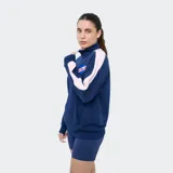 Buzo deportivo azul marino con medio cierre frontal, cuello alto y bandas rosadas en las mangas. Presenta el logo de Umbro y el escudo del Club Nacional de Football bordados en el pecho, además de un bolsillo tipo canguro.